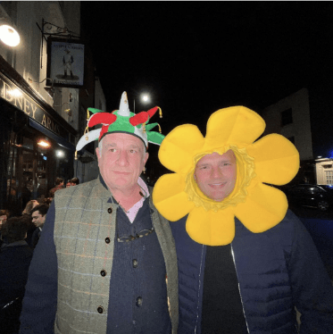 Two men wearing a yellow flower and a jester's hat.